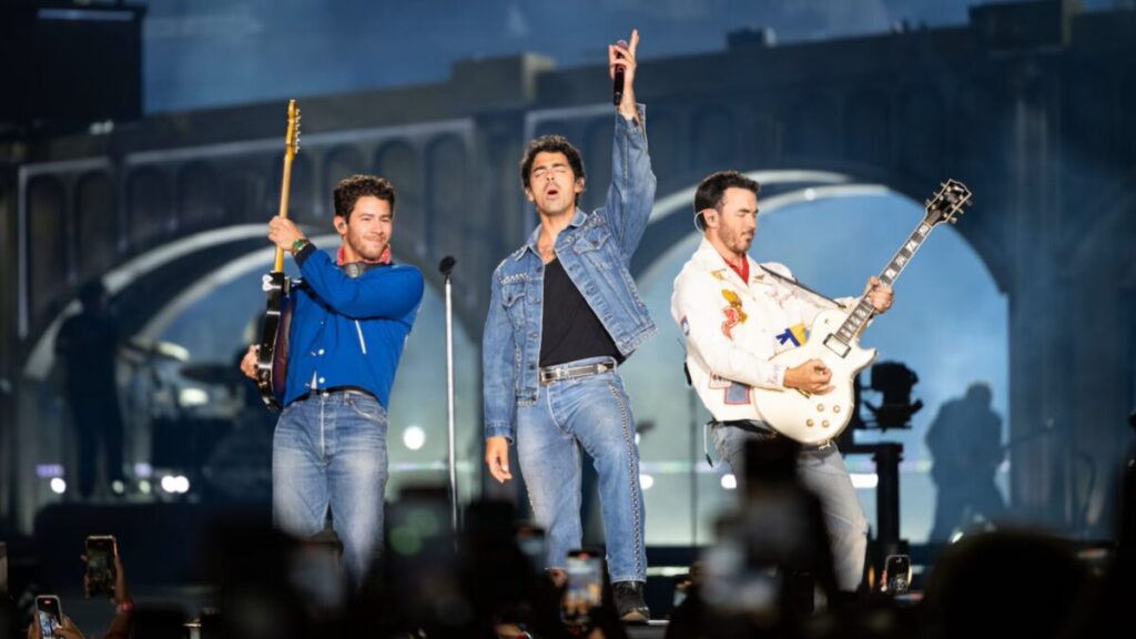 Jonas Brothers en concierto en el Amerant Bank Arena de Sunrise, Florida, con luces y público celebrando 20 años de carrera musical.