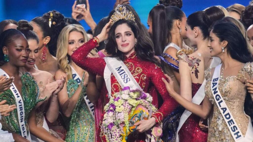 Fátima Bosch coronada en Miss Universo en un escenario iluminado en Bangkok, rodeada de participantes, en medio de cuestionamientos por escándalos recientes.