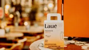 Caja 4-pack de Laué Frizzante sobre una mesa en ambiente urbano con luces cálidas y escenario de restaurante al fondo.