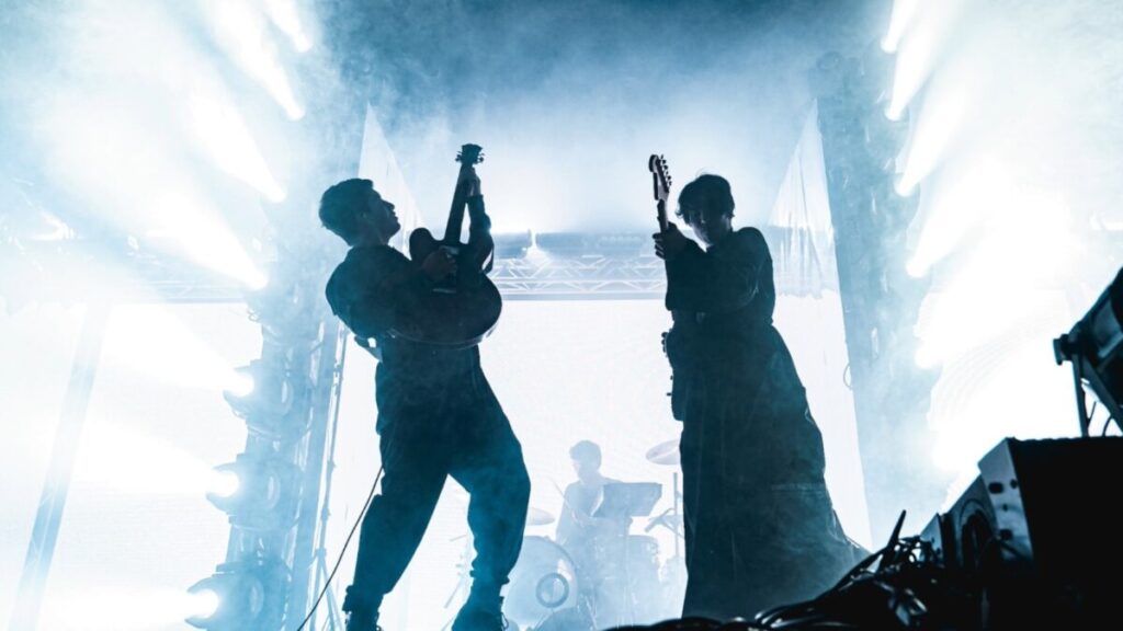 El dúo argentino Peces Raros en un escenario al aire libre con luces verdes y azules durante su presentación en Miami.