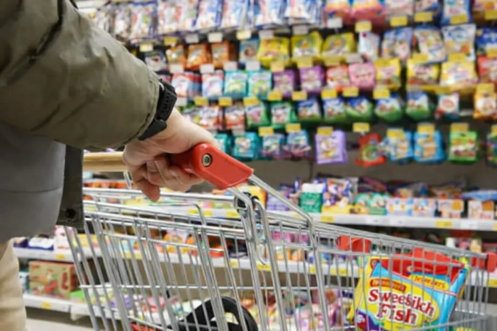 Carrito de compras frente a estante lleno de dulces infantiles, alerta por arsénico en dulces comunes en Florida
