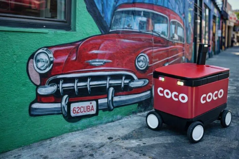 Robot de entregas Coco en Miami junto a mural urbano con auto clásico, símbolo de innovación y cultura latina