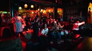 Aficionados ven el Super Bowl en Miami en bares y cervecerías con pantallas gigantes, bebidas, comida y ambiente festivo nocturno.