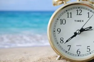 Vista de un reloj en primer plano con fondo de la ciudad de Miami al atardecer, representando el cambio de horario en marzo 2026