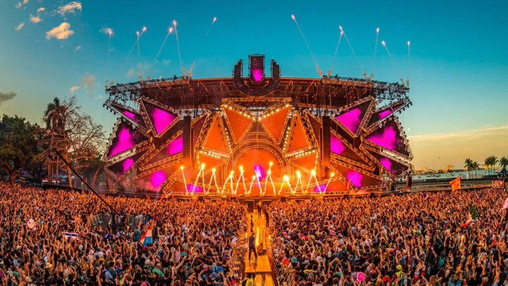 DJ tocando música electrónica frente a público en club nocturno de Miami con luces y ambiente festivo