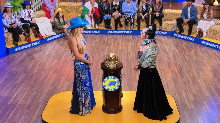 Natalia Alcocer con sombrero azul e Ivonne Montero con chaqueta plateada, frente a frente junto a una corona en La Granja VIP.
