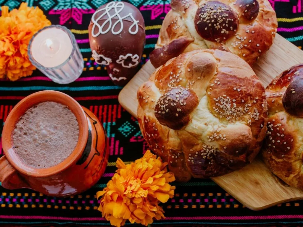 Pan de muerto tradicional mexicano cubierto de azúcar y decorado con figuras de huesos, acompañado de flores de cempasúchil.